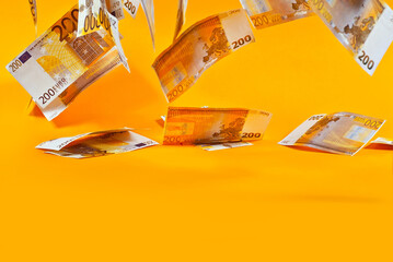 Yellow dollar bills on an orange background. 200 euro banknotes close up. Money flies in the air....