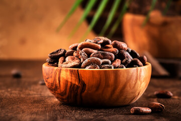Unpeeled organic cocoa bean in bowl on wooden rustic table background. Copy space