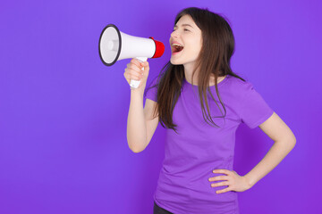 Fototapeta na wymiar Funny young beautiful Caucasian girl wearing purple T-shirt over purple background People sincere emotions lifestyle concept. Mock up copy space. Screaming in megaphone.