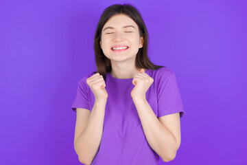 young beautiful Caucasian girl wearing purple T-shirt over purple background grins joyfully, imagines something pleasant, copy space. Pleasant emotions concept.