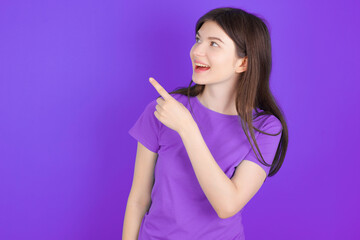 young beautiful Caucasian girl wearing purple T-shirt over purple background glad cheery demonstrating copy space look novelty