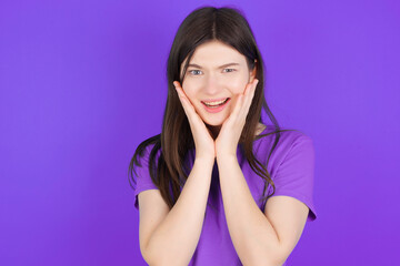 Upset young beautiful Caucasian girl wearing purple T-shirt over purple background touching face with two hands