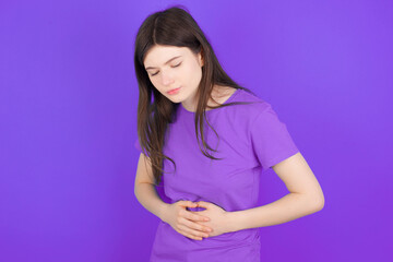 Fototapeta premium young beautiful Caucasian girl wearing purple T-shirt over purple background got stomachache