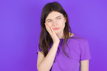 young beautiful Caucasian girl wearing purple T-shirt over purple background with toothache
