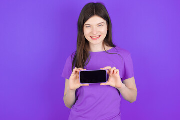 Naklejka premium Cheerful cheery content young beautiful Caucasian girl wearing purple T-shirt over purple background holding in hands device hobby smm post blog