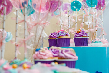 Lilac cupcakes and long lollipops with ribbons on a blue stand.