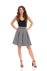 Young Woman In Striped Skirt And High Heels Is Standing With Hands On Hip