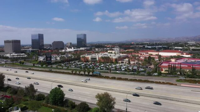 Aerial drone footage of a densely-populated urban city in Southern California with skyscrapers and a busy freeway on a sunny day.