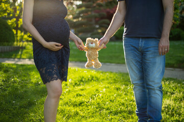 Junge schwangere Frau hält mit Ihrem Mann ein Teddybär mit den Händen. Romantische Aufnahme 

