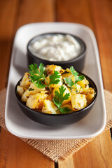 Close-up of Indian vegetarian dish of spicy Potato and Tomato curry garnished with green coriander fresh leaves with curd. Served in a black ceramic bowl over wooden background.
