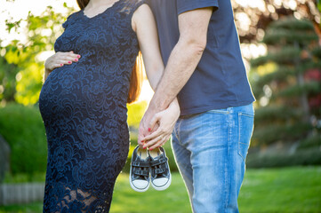 Schwangere Frau mit Partner h&auml;lt Babyschuhe &ndash; Vorfreude auf das Baby