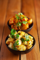 Close-up of Indian vegetarian classic combination of dishes  Jeera Aloo (Potatoes in cumin Flavored ) and spicy Potato and Tomato curry garnished with green coriander fresh leaves.