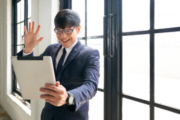 Fototapeta premium Asian businessman smile and say hi with tablet in home office