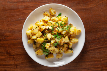 Close-up of Indian vegetarian classic dish Jeera Aloo - Potatoes Flavored with Cumin garnished with green coriander fresh leaves. Served in white ceramic plate over wooden background
