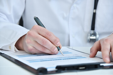 Fototapeta premium Doctor hand filling patient history list at clipboard.