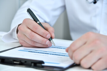 Fototapeta premium Doctor hands writing on clipboard in medical office