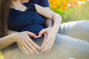 Eine schwangere Frau sitzt in einer Blumenwiese und wird von ihrem Partner liebevoll umarmt. Er...