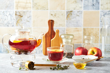 Fruit tea with apples and thyme in glass teapot and cup on the kitchen table