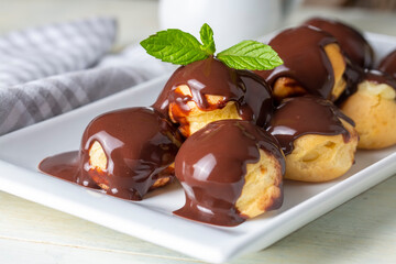 Delicious profiteroles with chocolate and white plate. Selective focus image on light background.