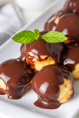 Delicious profiteroles with chocolate and white plate. Selective focus image on light background.