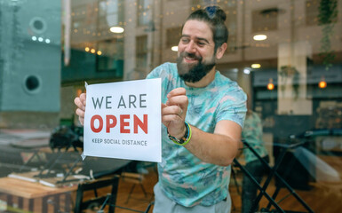 Happy man placing opening poster after coronavirus on the glass of his business