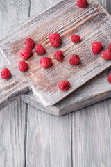 Raspberry fruits on old cutting board, healthy pile of summer berries on grey wooden background, angle view