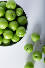 Fresh green plums in a white bowl. Top view.