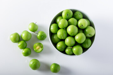Fresh green plums in a white bowl. Top view.