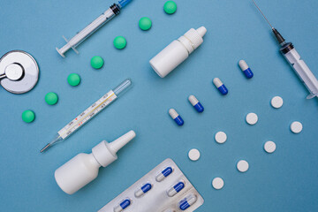 Medical layout of various medical equipment, pills, syringe, thermometer, nasal spray on a blue...