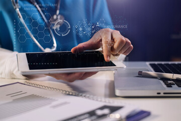 Doctor working on laptop computer and tablet and medical stethoscope on clipboard on desk.