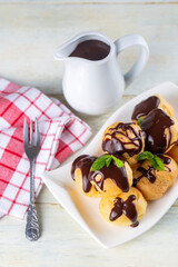 Delicious profiteroles with chocolate and white plate. Selective focus image on light background.