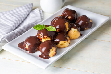 Delicious profiteroles with chocolate and white plate. Selective focus image on light background.