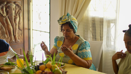 Elderly woman praying with family at breakfast table