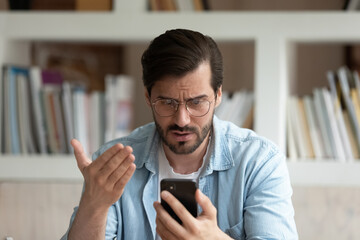 Close up unhappy irritated man in glasses looking at phone screen, worried businessman reading bad...