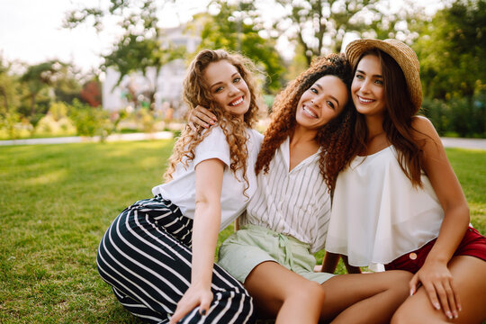 Three young woman relaxing on the grass. Young friends laughing and enjoying holidays together. Friendship, youth and travel concept.