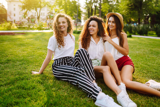 Three young woman relaxing on the grass. Young friends laughing and enjoying holidays together. Friendship, youth and travel concept.