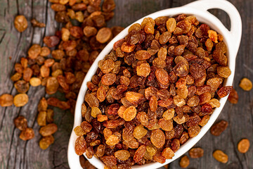 Raisins are beautifully dried highest grade in white bowl. Grape Raisins on wooden table top view