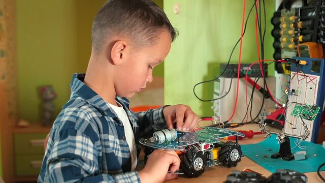 A boy in a workshop unscrews the screw on a toy car. He turns with his hand, remanufactures the wheel. Make a toy with your own hands. Favorite hobby.
