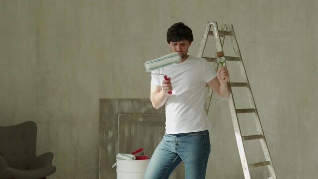 Funny man with a brush and roller dances, moves and sings during the renovation of the house.
