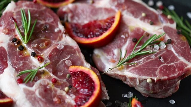 Fresh raw steaks with spices on a stone board. Marinated raw steaks with orange, rosemary and sea salt. BBQ meat.