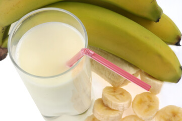 Verre de smoothie &agrave; la banane avec une paille et des bananes et coup&eacute;es en rondelles en gros plan