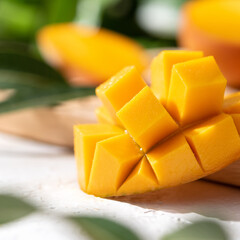 Diced fresh mango fruit on wooden cutting board with sunlight and leaf shadow.