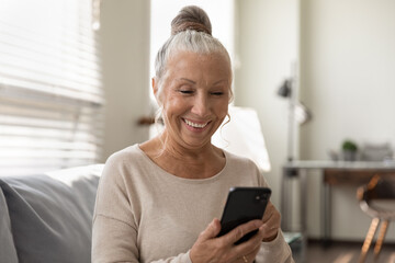 Elderly generation and modern tech. Smiling senior female use mobile phone app look at screen enjoy playing game. Happy aged woman retiree holding cell gadget chatting texting online watching video - obrazy, fototapety, plakaty
