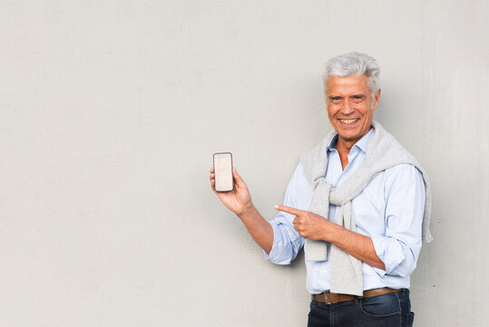 Smiling Older Man Holding Mobile Phone And Pointing Finger To Screen