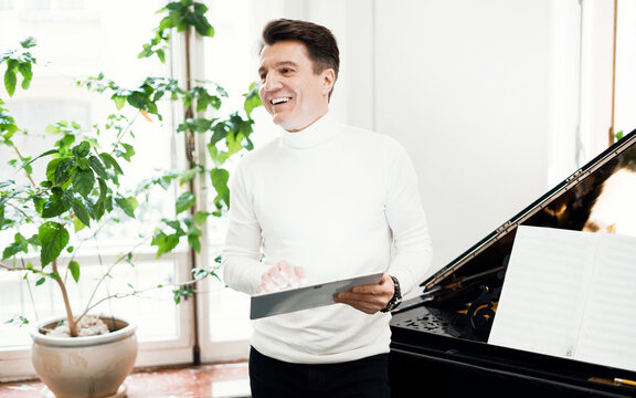 A gray-haired, positive man in age, writes down new cases on the project in the gadget. A confident person is a musician sitting near the piano. Portrait of a creative person smiling.