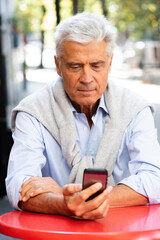 Obraz premium gray hair man sitting at table looking at mobile phone