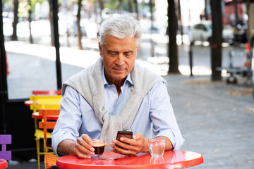 handsome older man sitting at cafe terrace looking at mobile phone