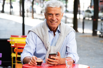 handsome gray hair man sitting outside cafe terrace with mobile phone