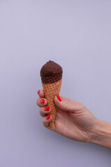 The hand of a fair-skinned girl with a red manicure is holding an ice cream against a purple background