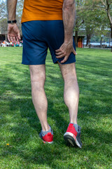 Senior athlete man with muscle pain during training outdoors. Thigh muscle cramps trauma. View from the back. Vertical orientation. - obrazy, fototapety, plakaty